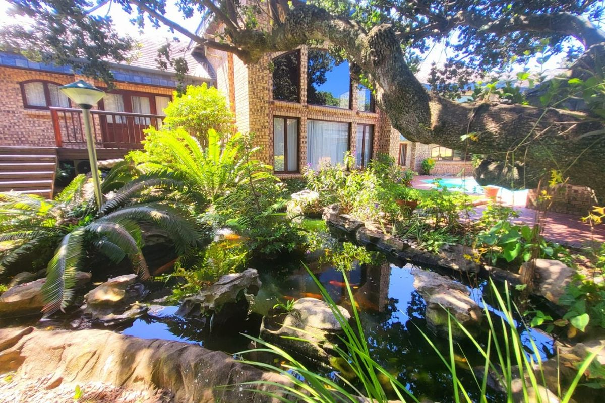 A landscaped rear garden featuring a large koi pond, mature trees, a swimming pool, and a brick-faced residence with a timber deck.