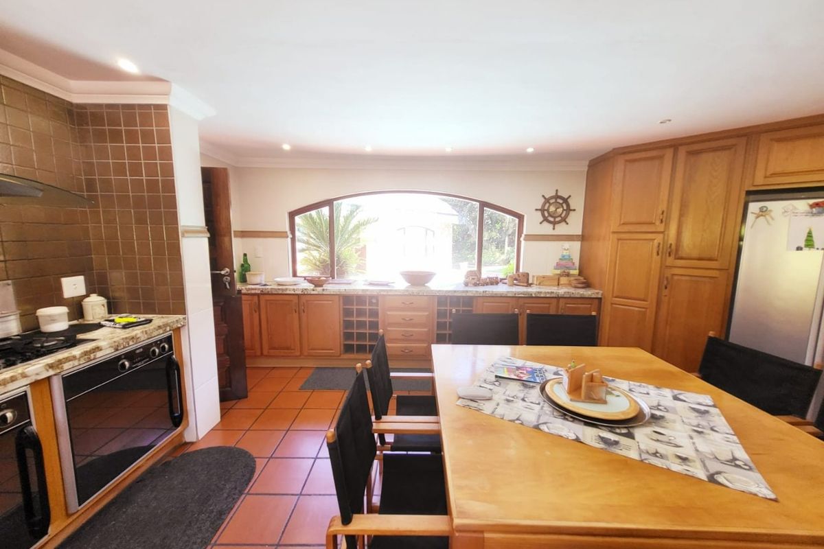 Spacious kitchen featuring warm-toned wooden cabinetry, granite countertops, built-in oven, gas hob, and a large arched window providing natural light.