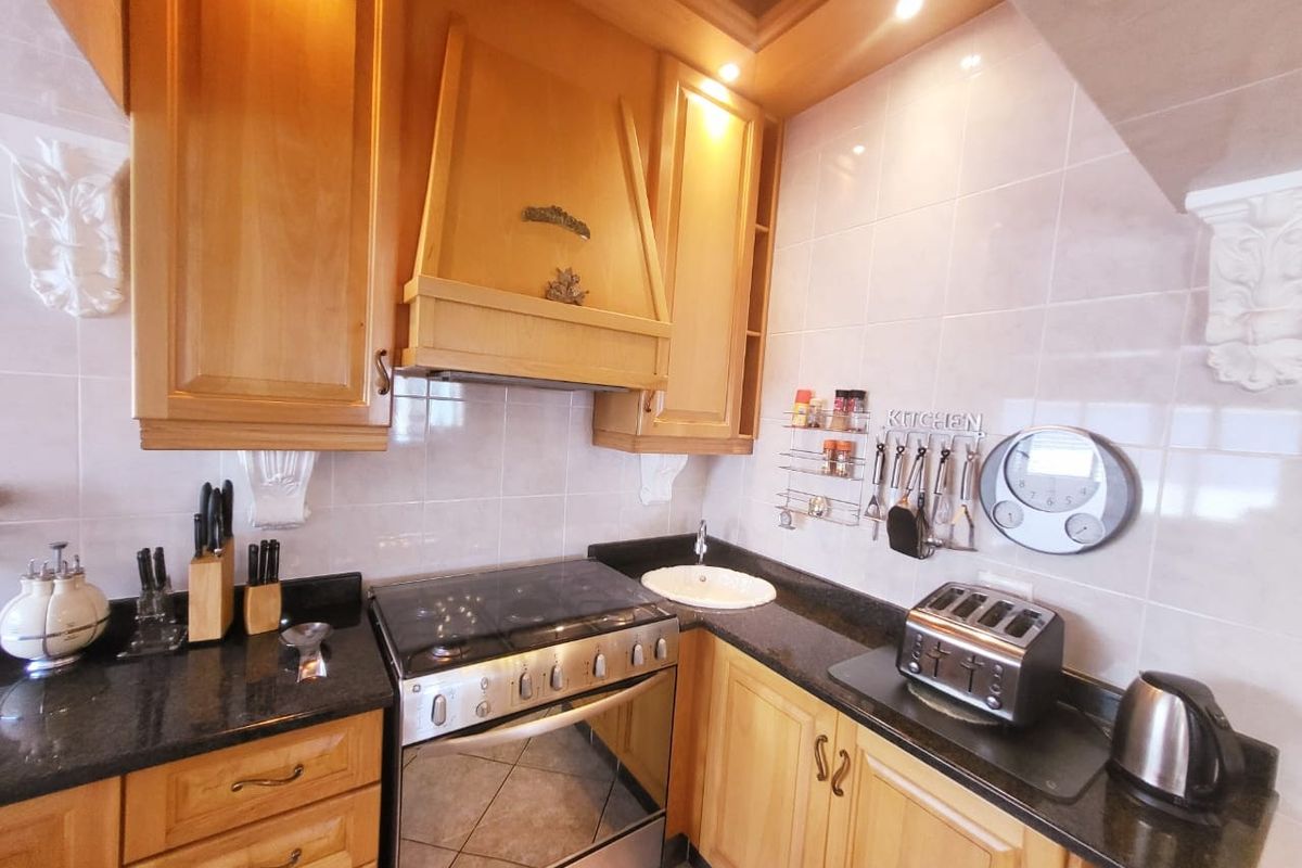 A functional kitchen featuring wooden cabinetry, granite countertops, a stainless steel gas stove with an integrated extractor hood, and a tiled backsplash.