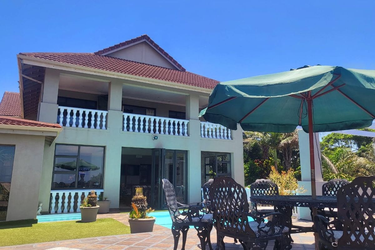 Rear view of a two-story house featuring a balcony with balustrades, a paved patio area, and a swimming pool.