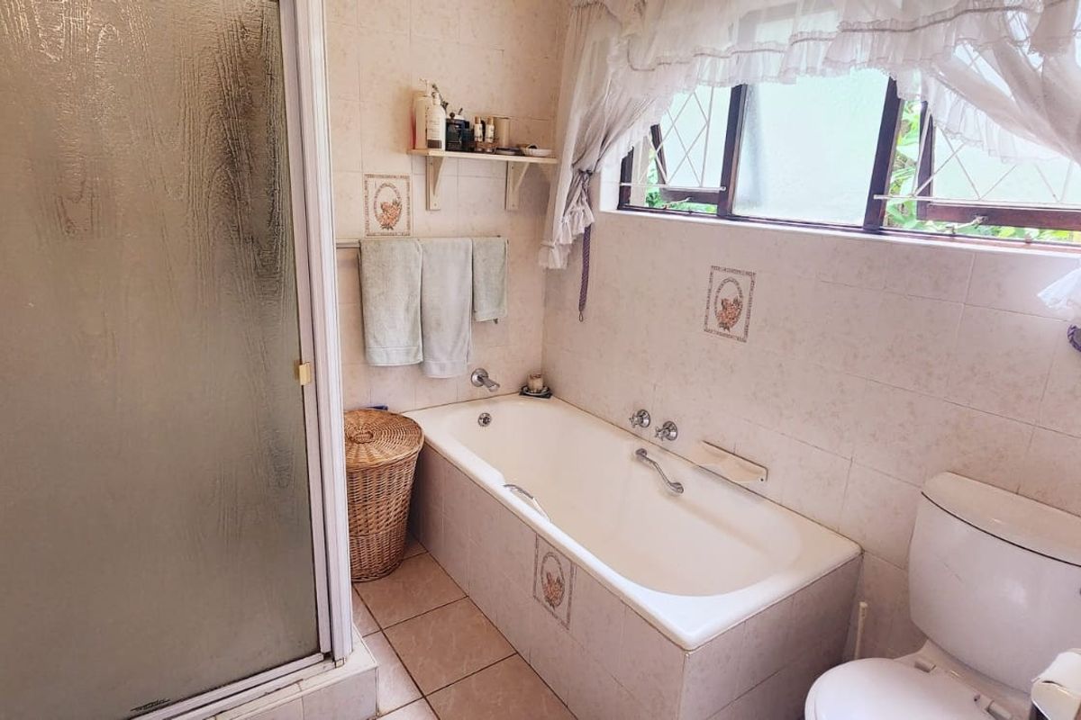 A functional bathroom featuring a built-in bathtub, separate shower enclosure, and toilet, finished with dated wall and floor tiles.