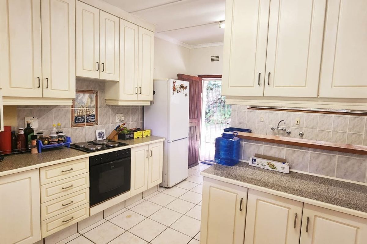 A functional kitchen featuring ample built-in cabinetry, laminate countertops, an integrated oven and hob, and tiled flooring with direct access to the exterior.