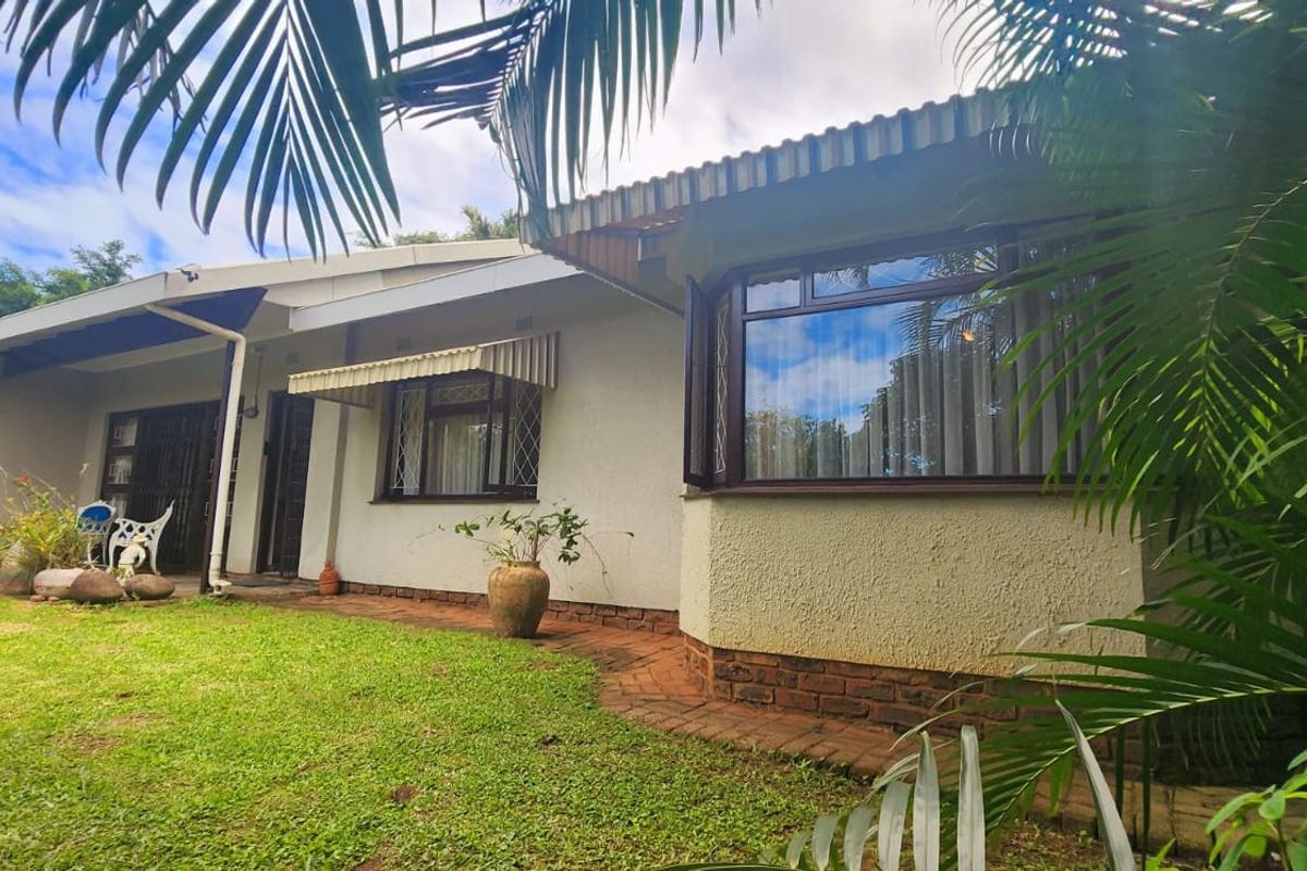 Rear view of the house featuring a lawn, brick pathway, and a prominent bay window with a tiled roof.