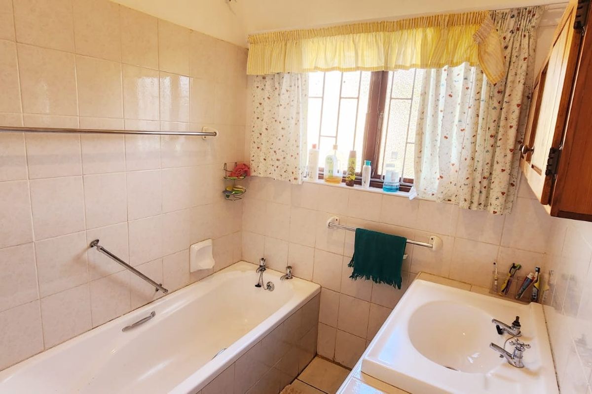 A functional bathroom featuring a bathtub, wall-mounted basin, and tiled walls, currently presenting in a dated condition.