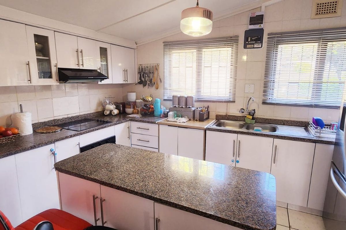 A functional kitchen featuring white cabinetry, granite countertops, a central island, and a double sink with tiled backsplash.