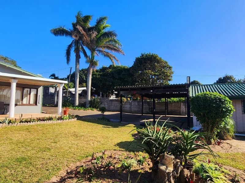 A spacious rear garden featuring a covered patio area, established palm trees, and a secondary structure with a corrugated metal roof.