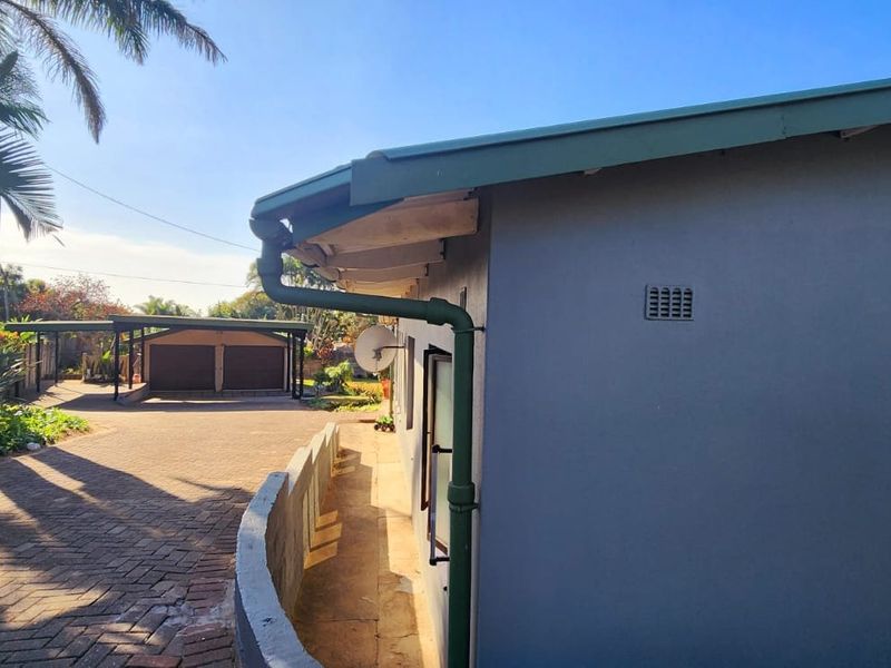 Side view of the property showing a paved driveway leading to a double carport and well-maintained exterior wall finishes.