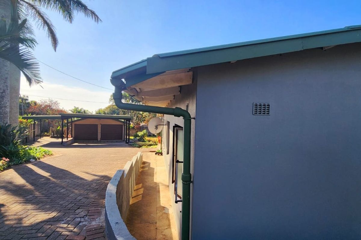 Side view of the property showing a paved driveway leading to a double carport and well-maintained exterior wall finishes.
