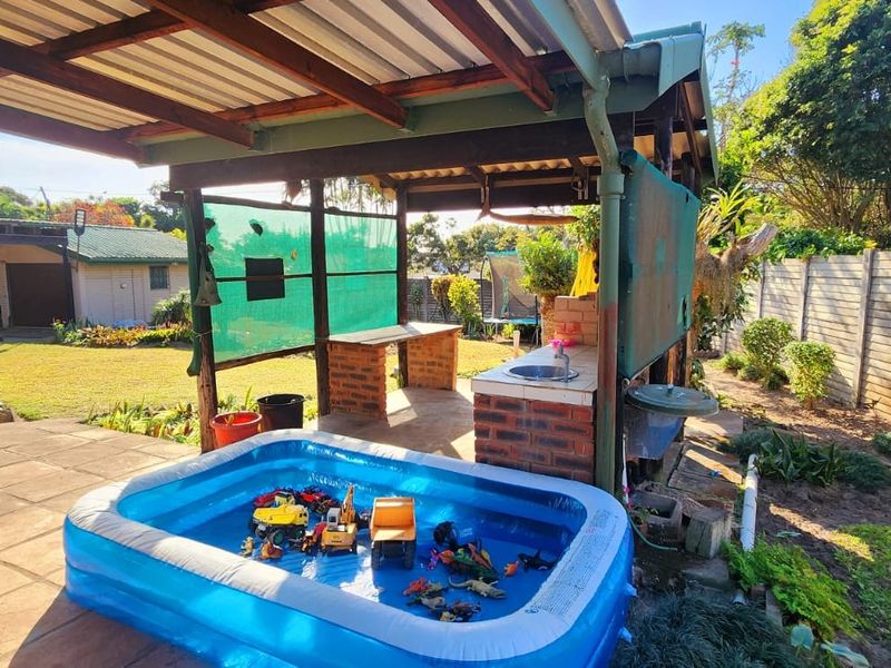 Covered outdoor patio area featuring a brick-built counter with a sink, overlooking a garden space with a precast concrete boundary wall.