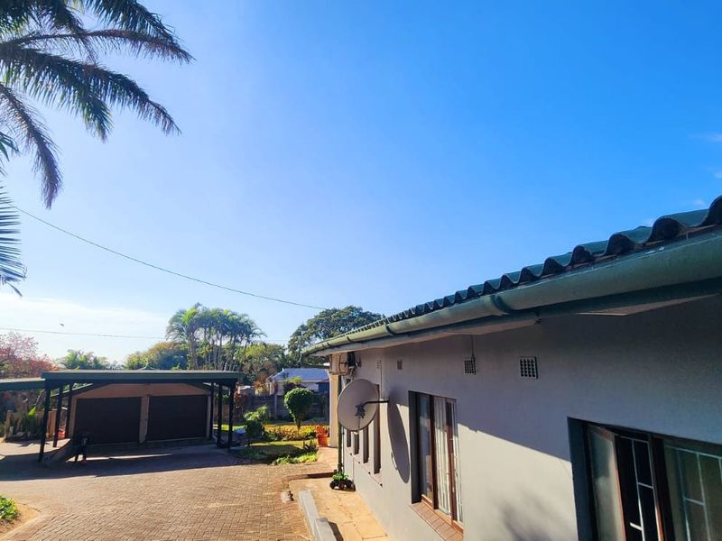 Rear exterior view of the property featuring a paved driveway, carport, and tiled roof structure.