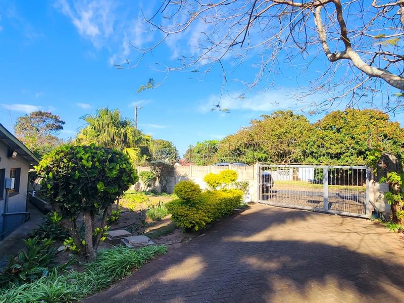 Front exterior view featuring a paved driveway, secure metal gate, perimeter wall with security spikes, and established garden area.