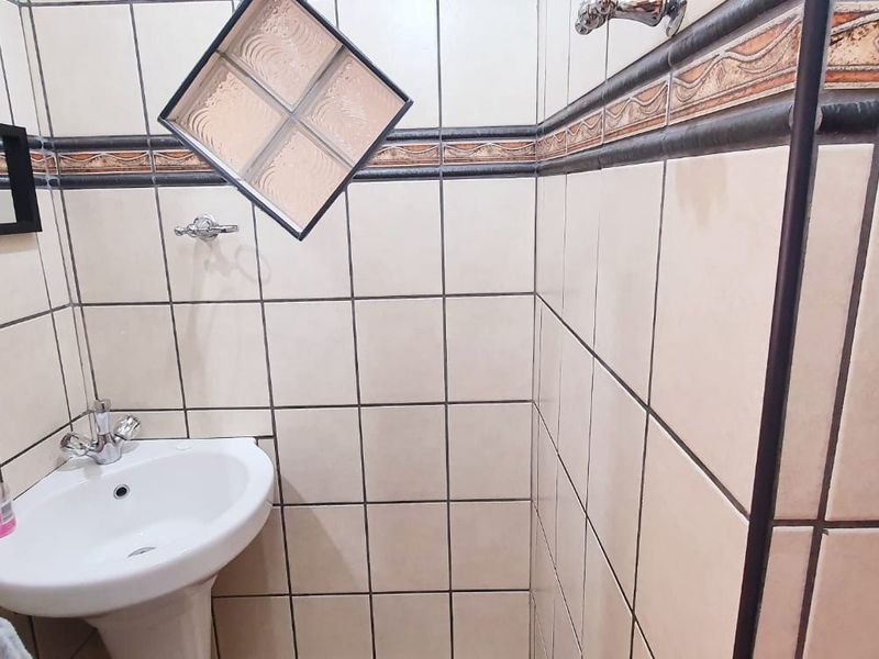 A compact bathroom featuring a pedestal basin, shower area, and dated wall tiling with a decorative border.