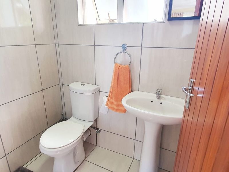 A compact guest bathroom featuring a pedestal basin, toilet, and neutral wall tiling.