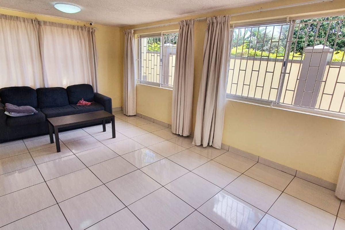 A living room featuring tiled flooring, large windows with security bars, and neutral wall finishes, offering a functional and well-lit space.