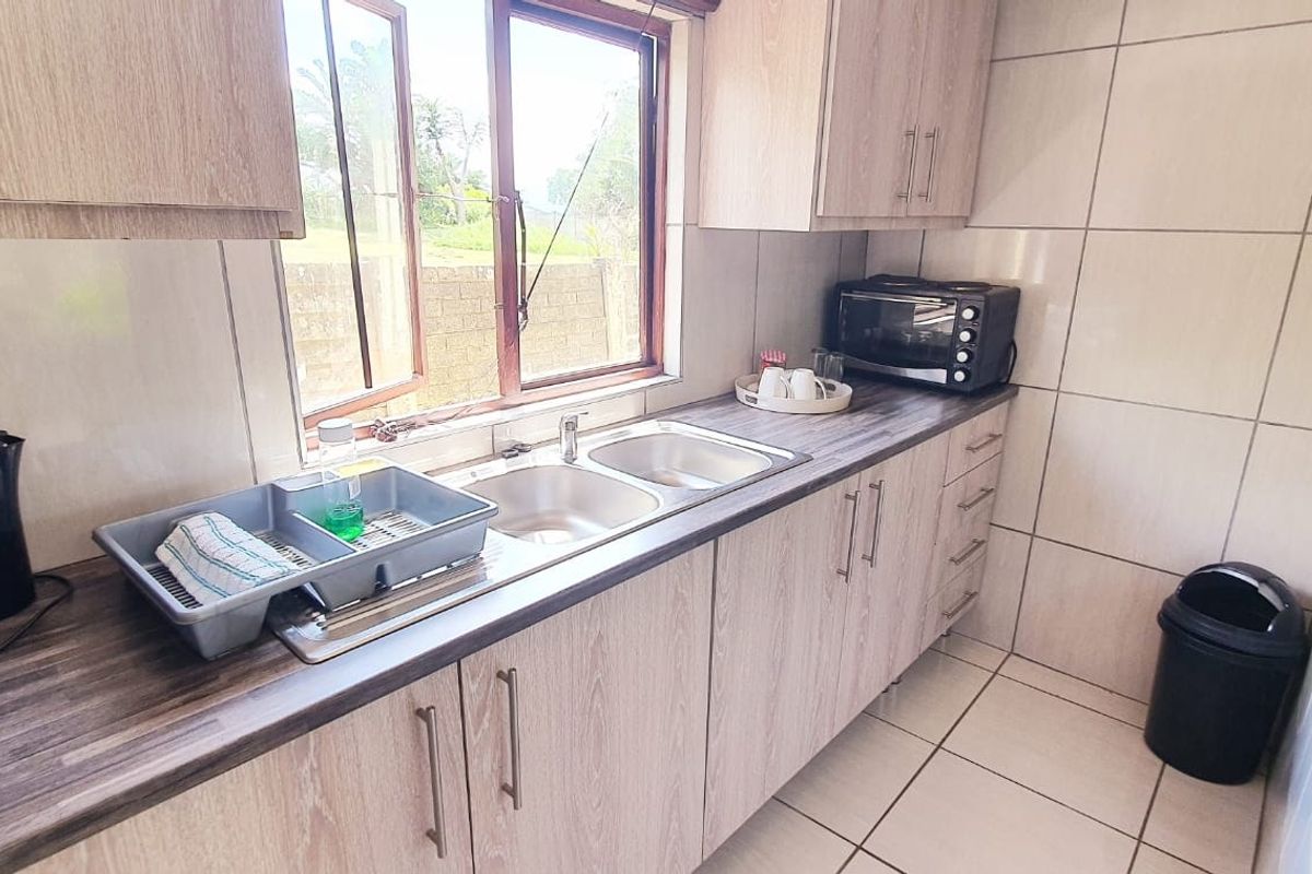 A functional kitchen featuring light wood-look cabinetry, laminate countertops, a double basin sink, and neutral wall and floor tiling.