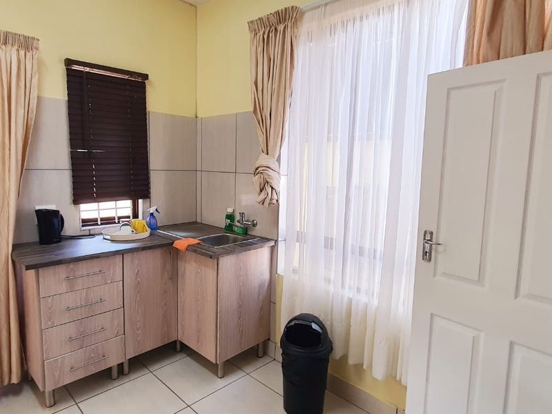 A functional scullery area featuring laminate countertops, stainless steel sink, tiled splashback, and timber-look cabinetry with tiled flooring.