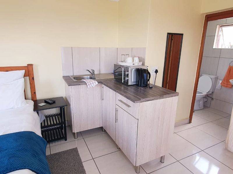 A bedroom featuring a compact kitchenette with cabinetry and sink, complemented by an adjoining en-suite bathroom with tiled flooring throughout.
