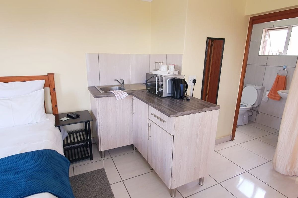 A bedroom featuring a compact kitchenette with cabinetry and sink, complemented by an adjoining en-suite bathroom with tiled flooring throughout.