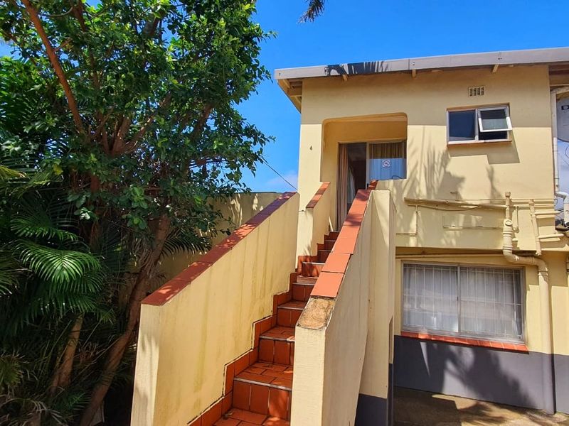 Rear exterior view of the property featuring an external staircase leading to an upper level, with visible wear to the exterior plaster and paintwork.