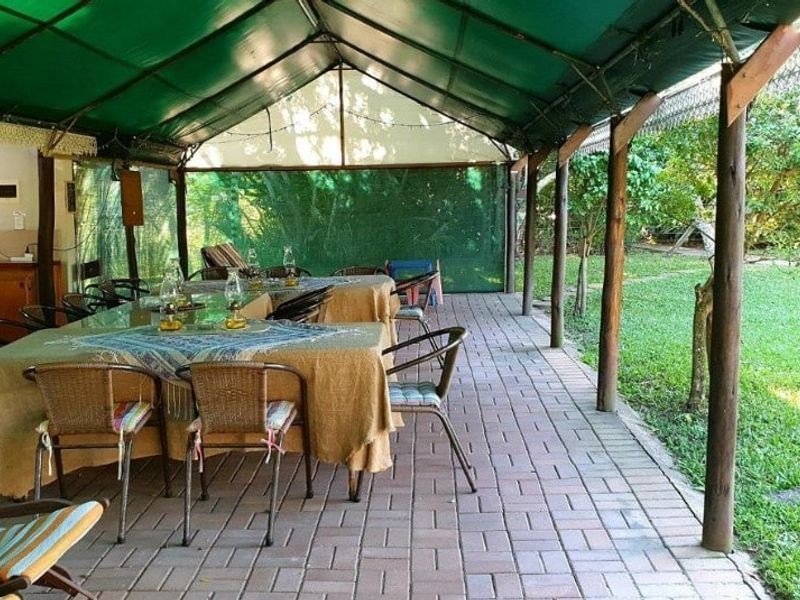 A covered outdoor patio area featuring paved flooring, timber support posts, and a green shade canopy, overlooking the garden.