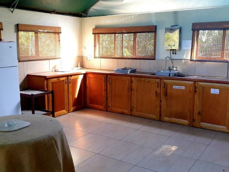 A functional kitchen area featuring timber cabinetry, tiled flooring, a stainless steel sink, and a wall-mounted gas geyser.