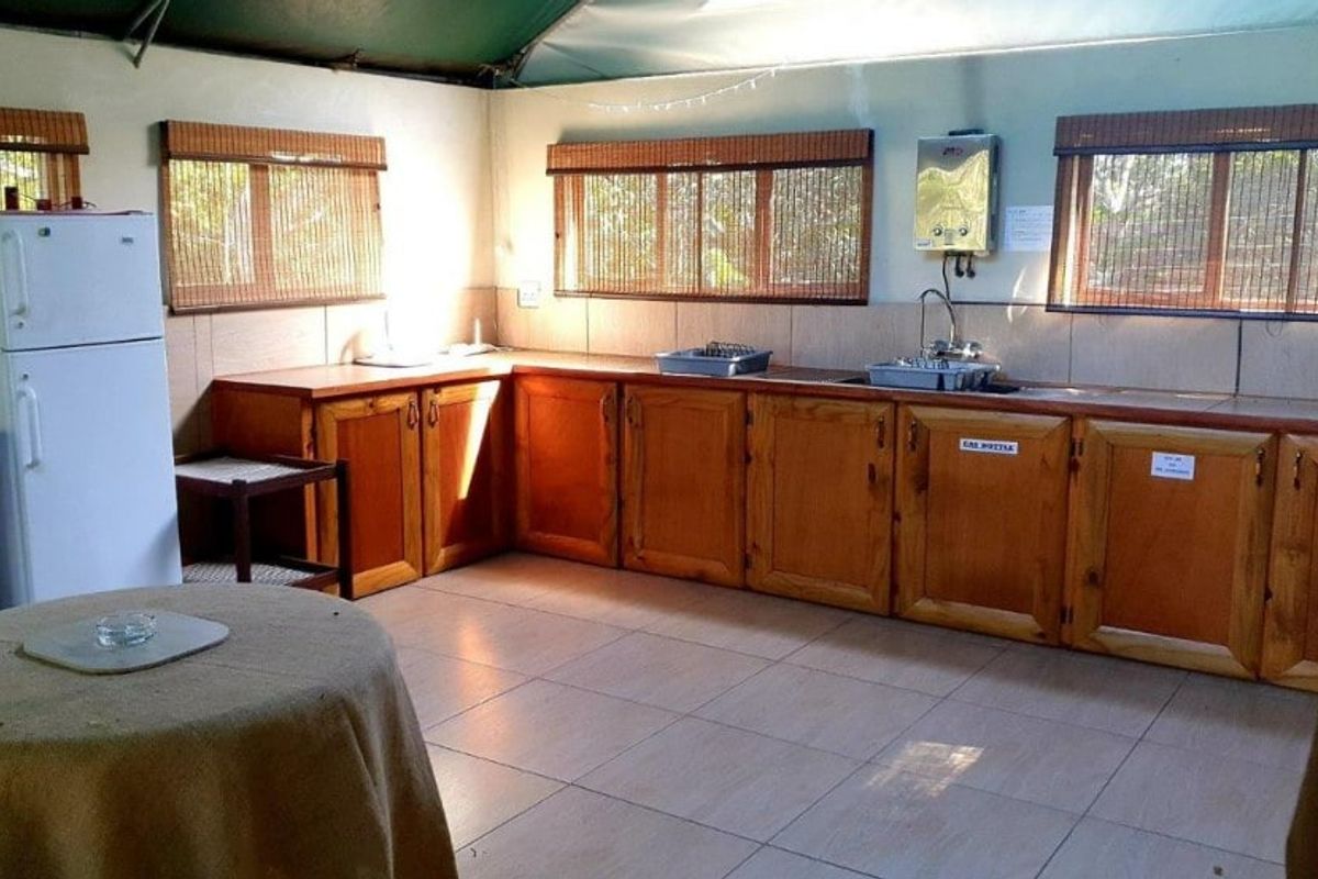 A functional kitchen area featuring timber cabinetry, tiled flooring, a stainless steel sink, and a wall-mounted gas geyser.