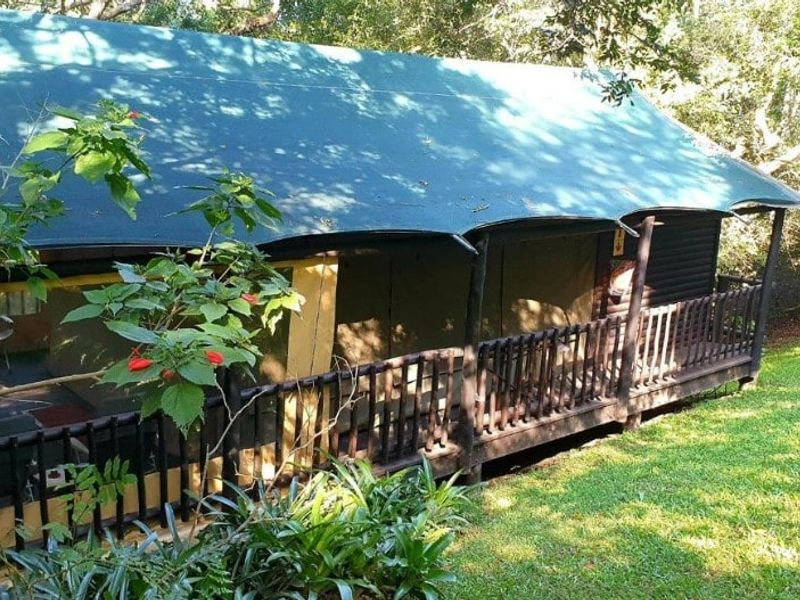 A rustic elevated timber deck with a canvas roof structure, offering an outdoor living space set within a natural garden environment.