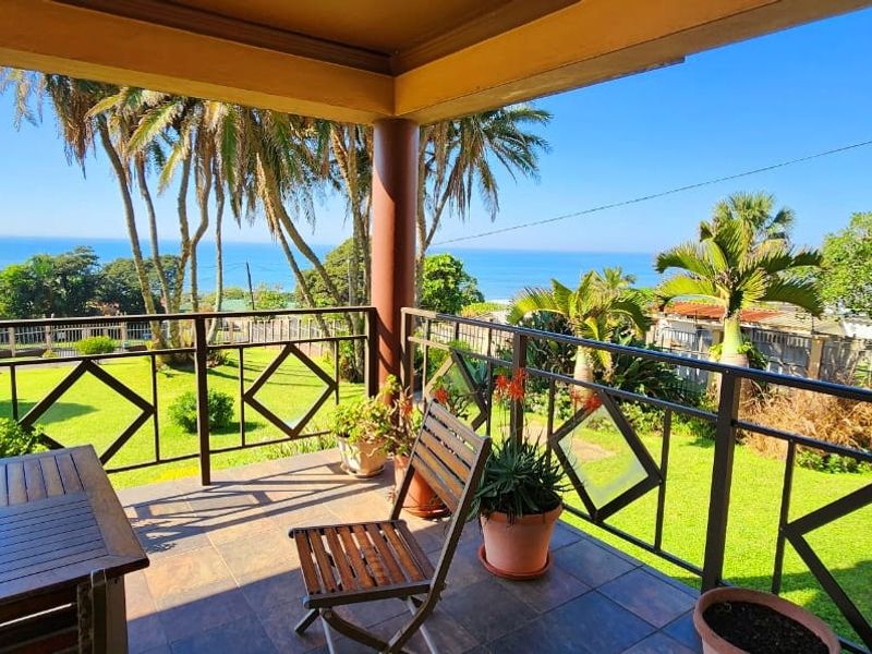 A covered patio featuring tiled flooring and a metal balustrade, offering expansive views of the garden and the ocean beyond.