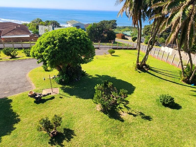 A spacious, well-maintained garden featuring a paved driveway, mature trees, and perimeter fencing, offering a pleasant outdoor space with coastal views.
