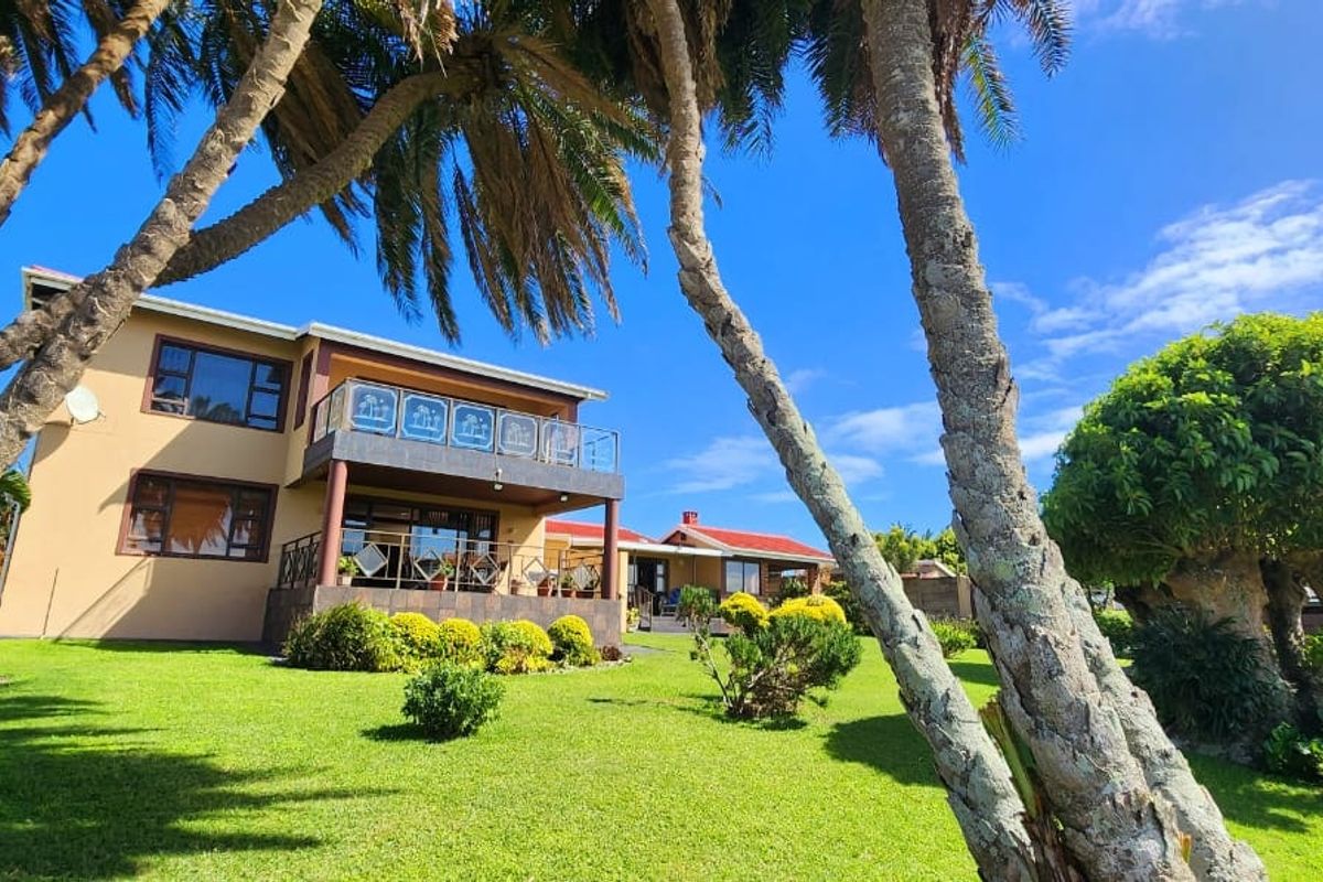 A view of the rear elevation of the house featuring a balcony with glass balustrades, set within a well-maintained landscaped garden.
