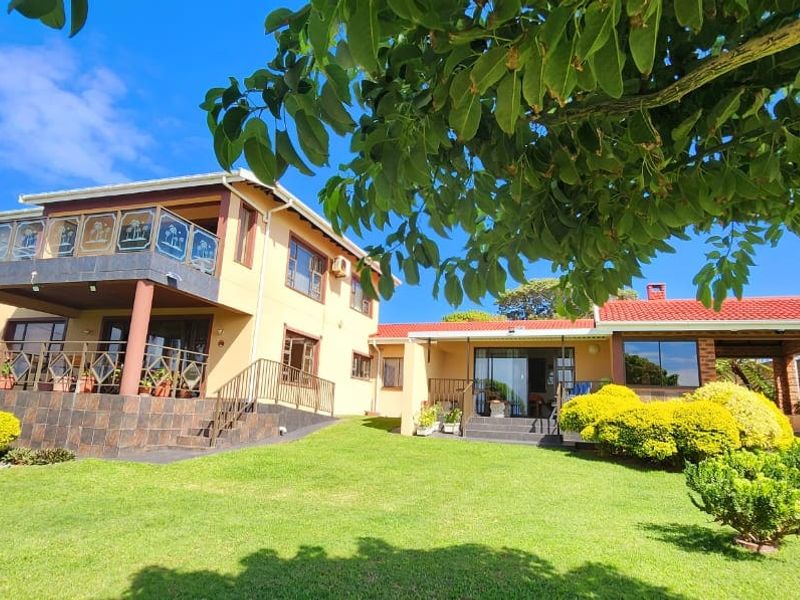 Rear view of a two-story house featuring a spacious lawn, a covered patio, and an upper-level balcony with glass railings.
