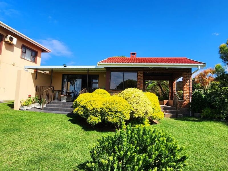 Rear view of the property featuring a well-maintained lawn, a covered patio area, and a multi-level building structure with a tiled roof.