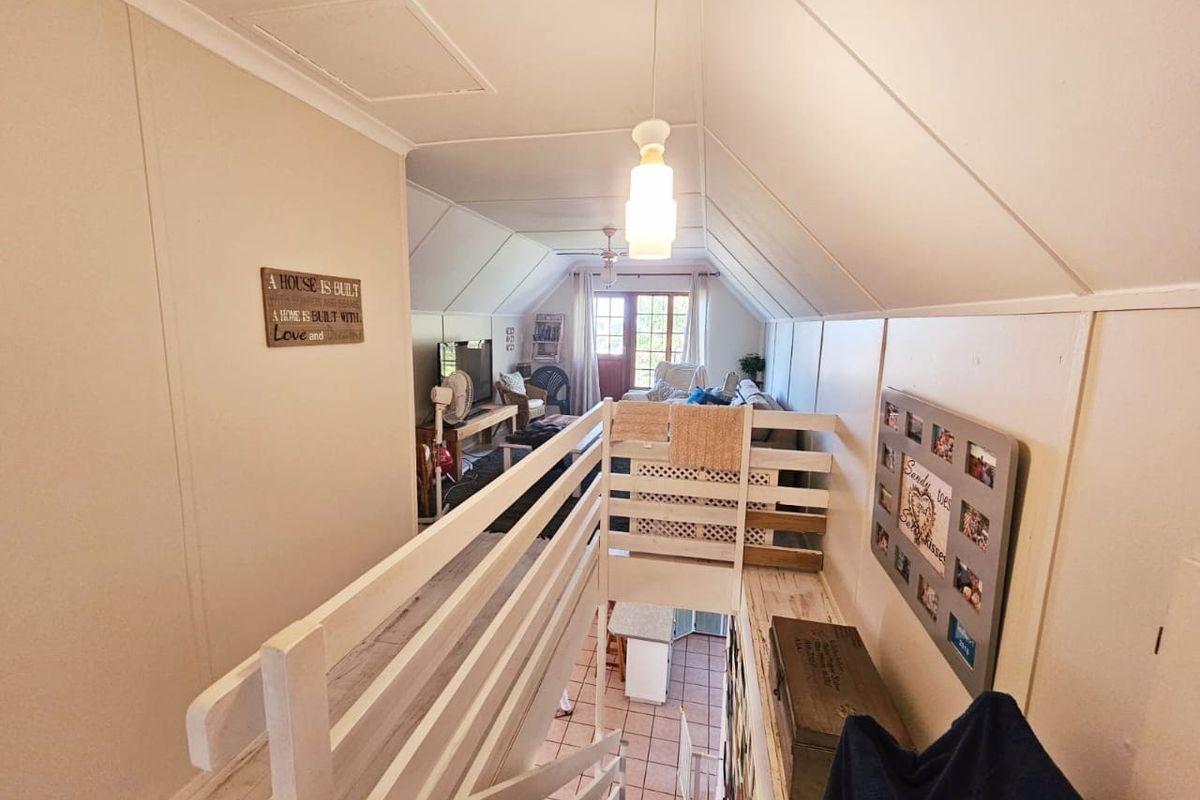 An elevated loft-style living area featuring a pitched ceiling, timber staircase with safety railing, and access to a lower level.