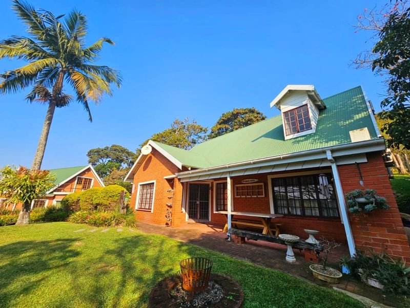 A charming brick house featuring a green corrugated metal roof, a dormer window, and a covered patio overlooking a well-maintained garden.