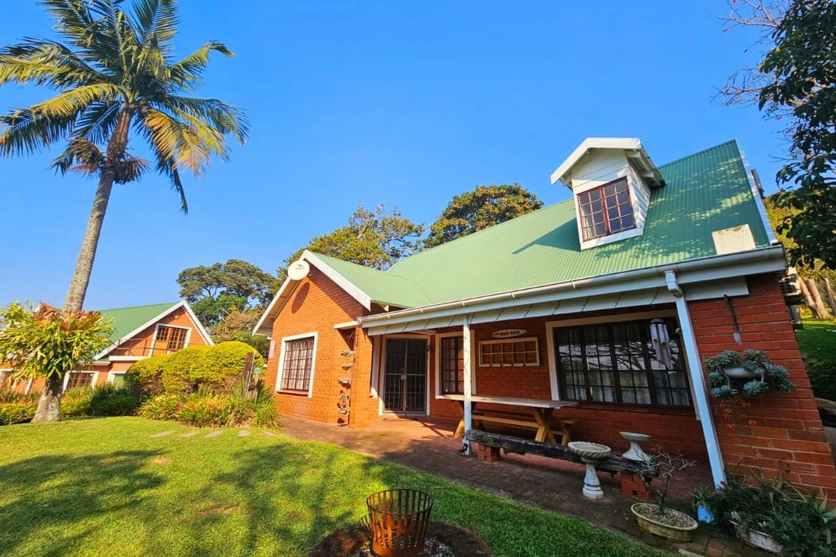 A charming brick house featuring a green corrugated metal roof, a dormer window, and a covered patio overlooking a well-maintained garden.