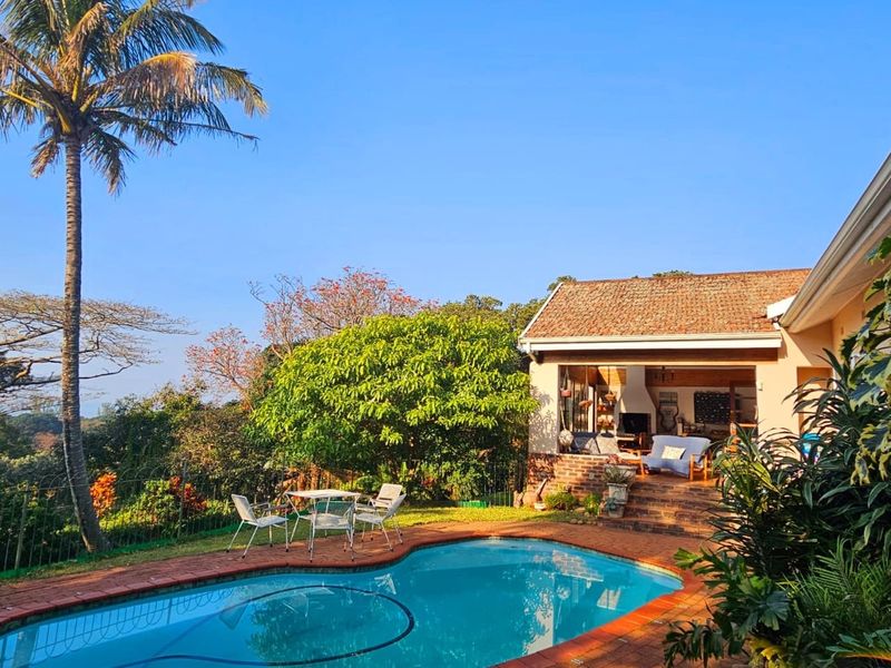 A well-maintained outdoor pool area featuring a brick-edged swimming pool, landscaped garden, and a covered patio space perfect for outdoor relaxation.