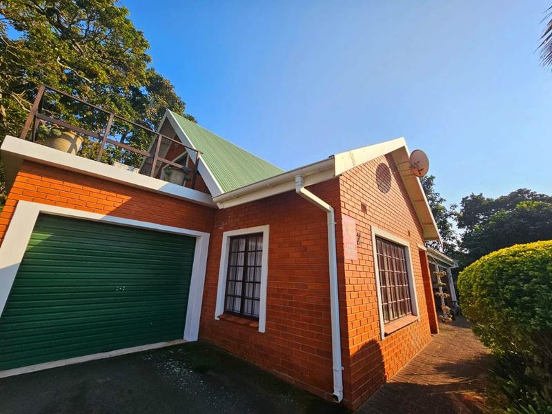 Front exterior view of a brick house featuring a green metal roof, a roller garage door, and an accessible roof terrace with railings.