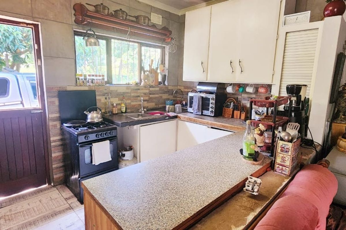 A functional kitchen featuring a gas stove, tiled backsplash, laminate countertops, and direct access to the exterior via a timber door.
