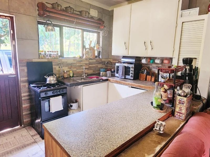A functional kitchen featuring a gas stove, tiled backsplash, laminate countertops, and direct access to the exterior via a timber door.
