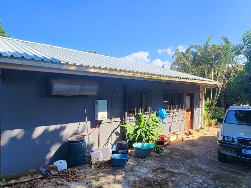 Rear exterior view of the property featuring a corrugated metal roof, external geyser, gas water heater, and security bars on the windows.