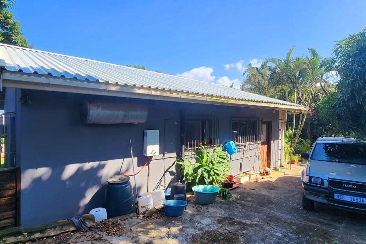 Rear exterior view of the property featuring a corrugated metal roof, external geyser, gas water heater, and security bars on the windows.