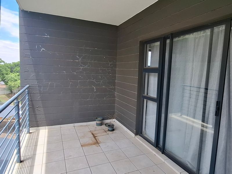 A balcony featuring tiled flooring, a metal balustrade, and a cladded feature wall, showing signs of wear and surface damage.