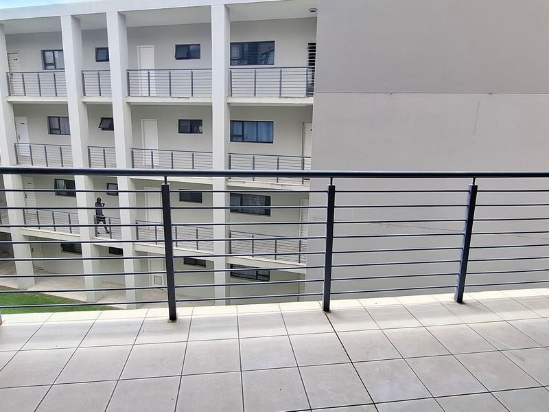 A clean, tiled balcony featuring a modern metal balustrade, overlooking the apartment complex courtyard.