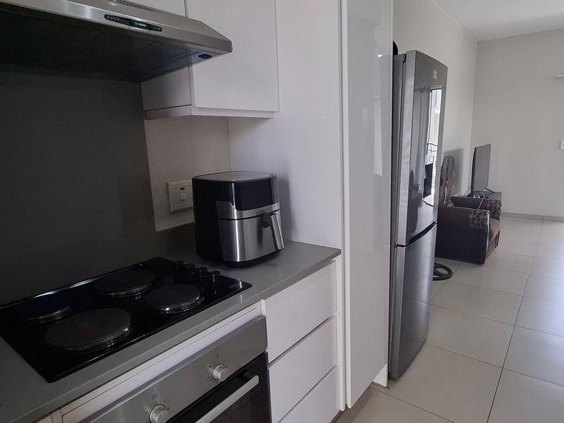 Modern open-plan kitchen featuring sleek cabinetry, integrated appliances, and tiled flooring, flowing seamlessly into the adjacent living area with balcony access.