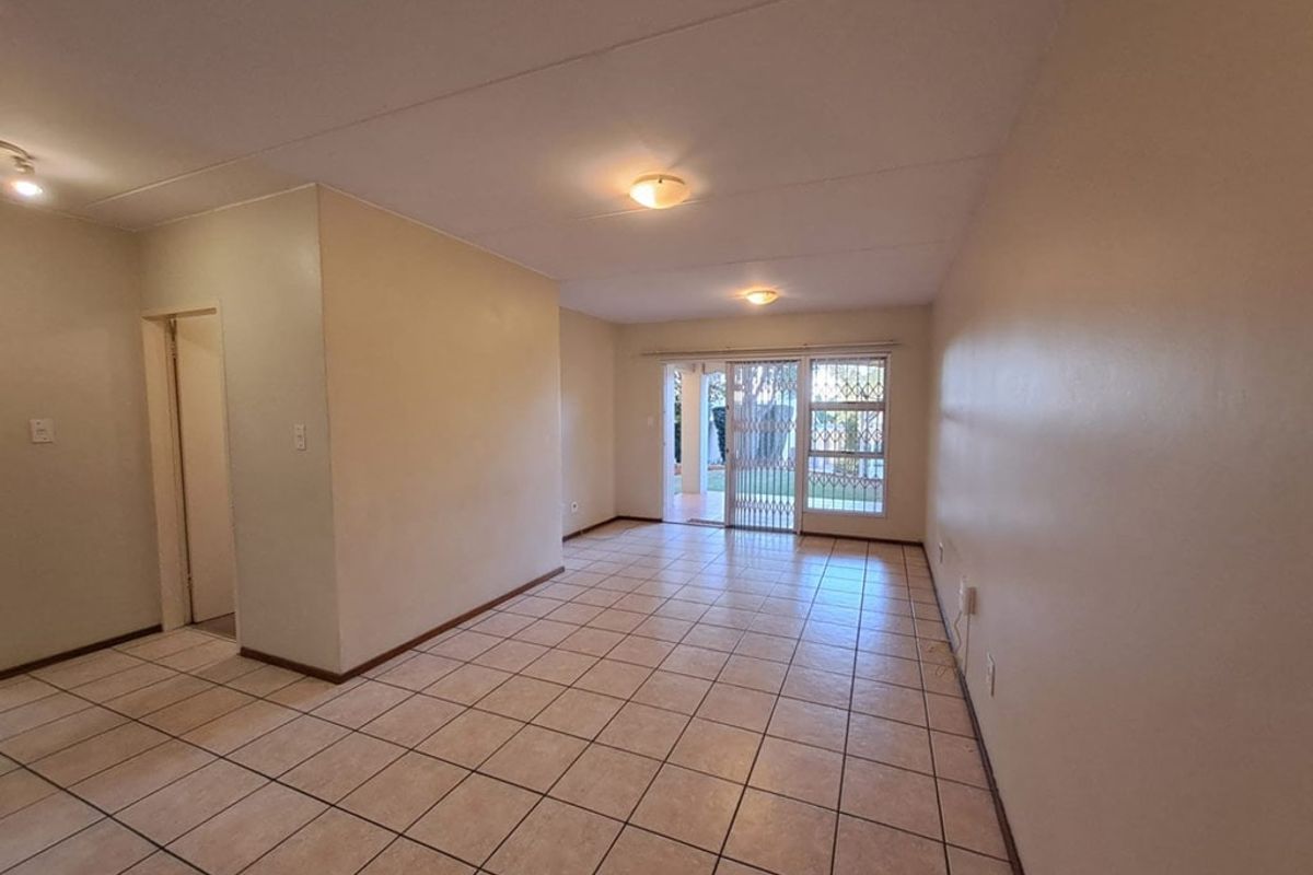A spacious, empty living area featuring neutral ceramic tile flooring, flush mount lighting, and a sliding glass door leading to an outdoor space.