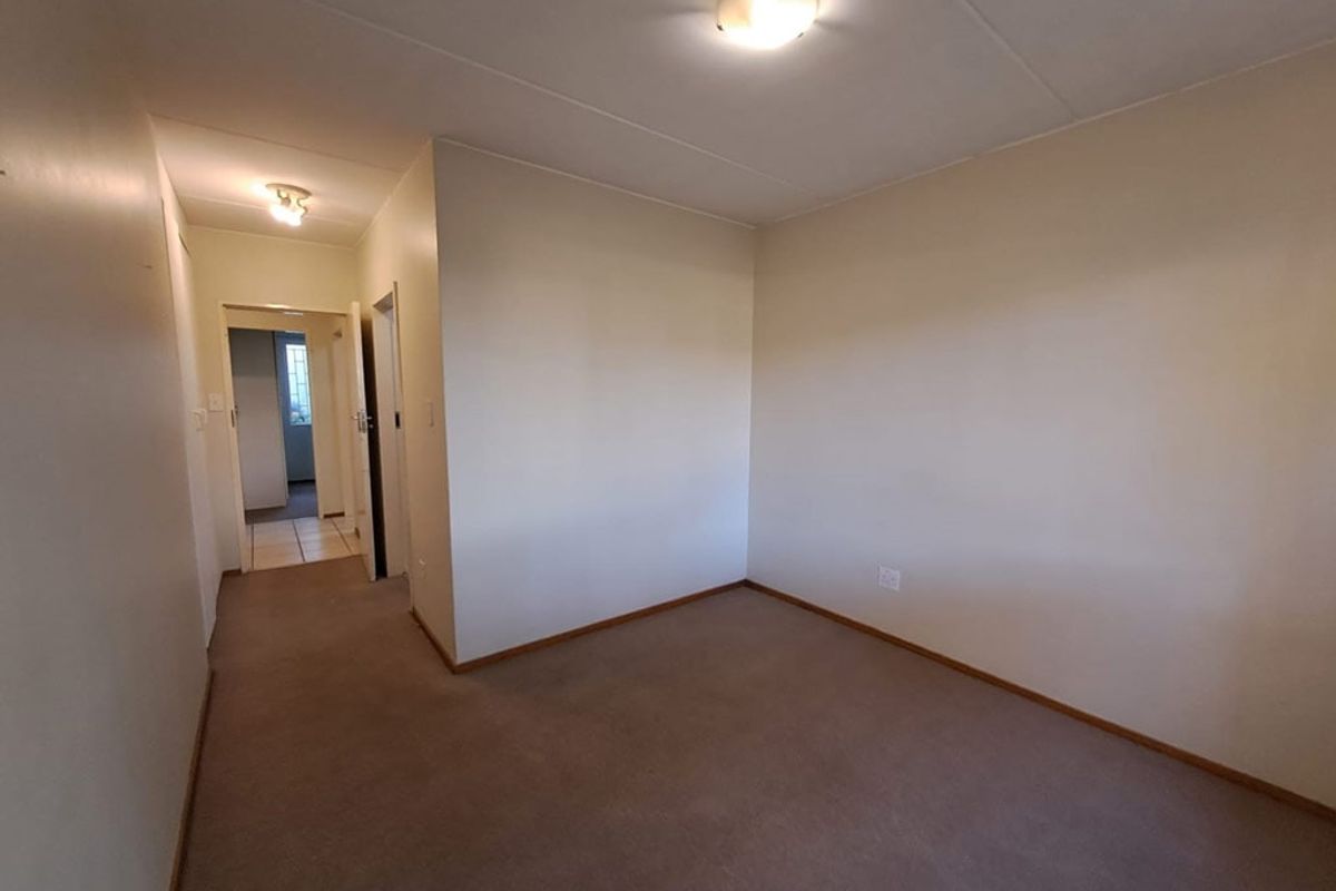 An empty bedroom featuring neutral walls, carpeted flooring, and flush mount ceiling lighting, with an adjacent hallway leading to another room.