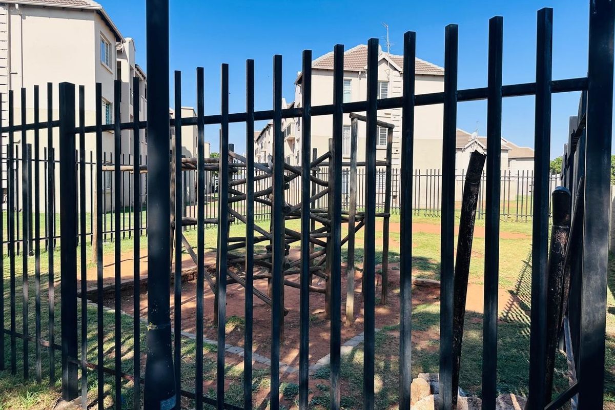 Communal outdoor area featuring a playground set within a fenced residential complex.