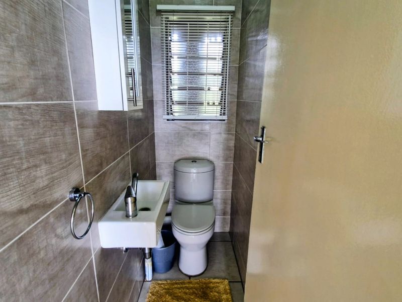 A compact guest bathroom featuring modern tiled walls, a wall-mounted basin, and a standard toilet.