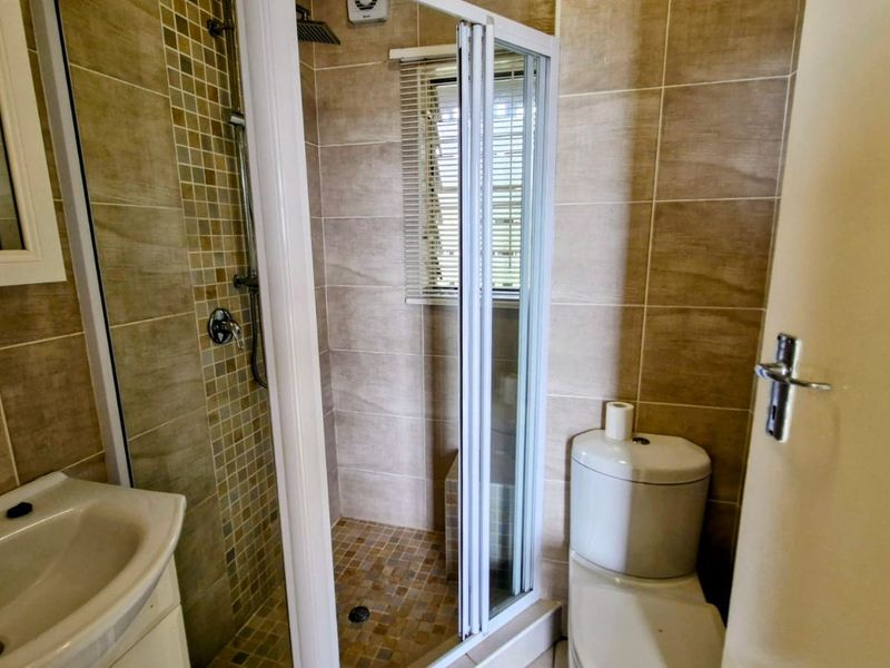 Compact bathroom featuring a shower enclosure with mosaic tiling, a pedestal washbasin, and a standard toilet with neutral wall tiles.