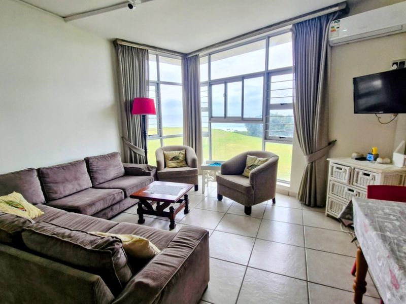 A bright living room featuring large windows with scenic views, tiled flooring, and a wall-mounted air conditioning unit.